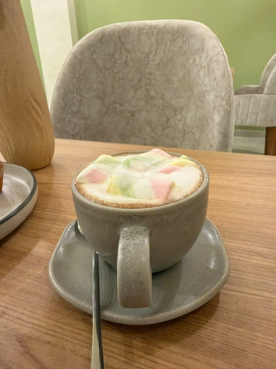 Latte con malvaviscos de colores en taza de gres sobre mesa de madera